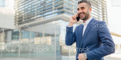 Young businessman posing in front of the building, talking on the phone and smiling